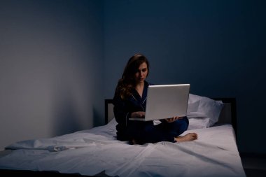 Uykusuzluk ve uykuda duygu ve evde yatakta oturan bir dizüstü bilgisayar üzerinde çalışan acı kadının resmi.