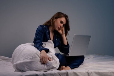 Gece yatakta bilgisayar ile oturan evde yorgun kadın resmi.