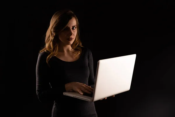 Curly hair woman holding laptop isolated over the dark background.