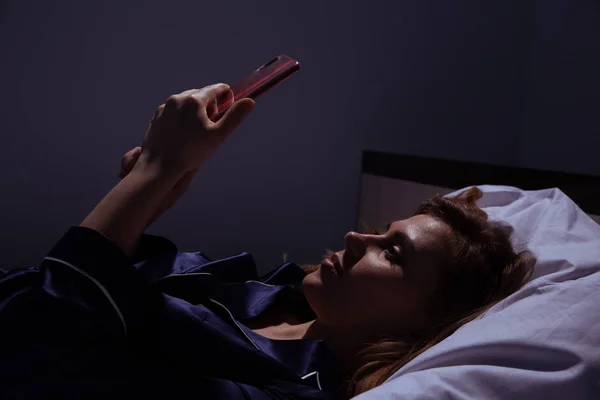 Woman at home with phone in the bed. Using mobile before going to sleep.