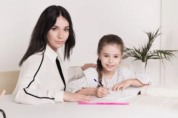 Mother and daughter sitting at the desk doing homework together. — Stock Photo, Image