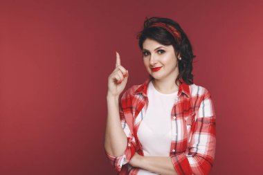Çekici kadın stüdyoda kırmızı arka planda parmağını bir şey işaret.
