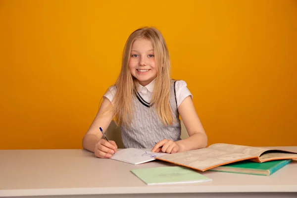 Счастливый ребенок делает домашнее задание сидя изолированы ярко-желтый фон . — стоковое фото