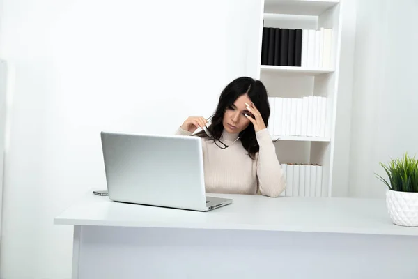 Sad and stressed woman in office sitting at the table and working till late.