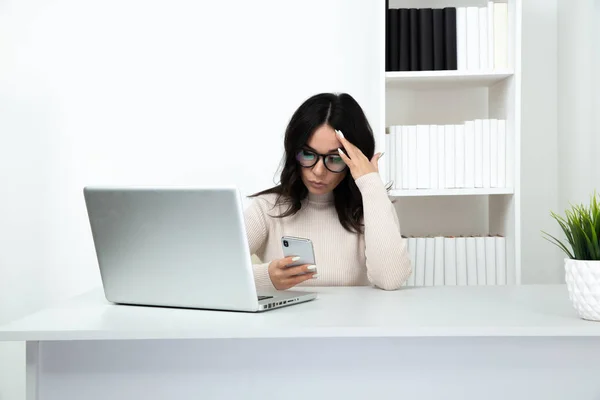 Unhappy and frustrated lady watching phone in office sitting infront of the computer.