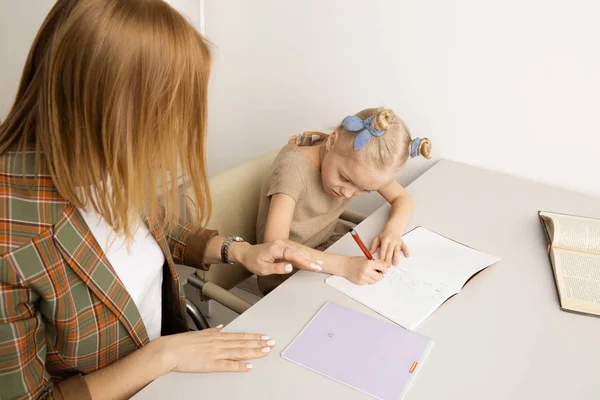 Sorrindo mãe com daugter sentados juntos na mesa e fazendo lição de casa . — Fotografia de Stock