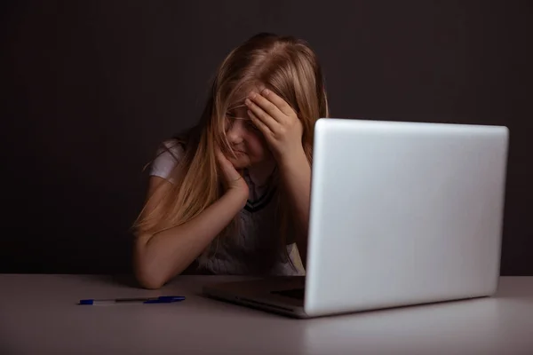 Lány fejfájás ül az íróasztalon, és csinál házi feladatot elszigetelt. Fáradt gyermek segítségével a számítógép. — Stock Fotó