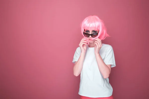 Retro divat koncepció. Nő rózsaszín hajú, fekete pohár és fehér T-shurt egy élénk rózsaszín stúdióban. — Stock Fotó