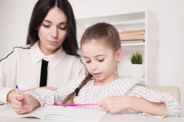 Bonito concepto familiar. Mamá e hija sentadas juntas y estudiando en casa . — Foto de Stock