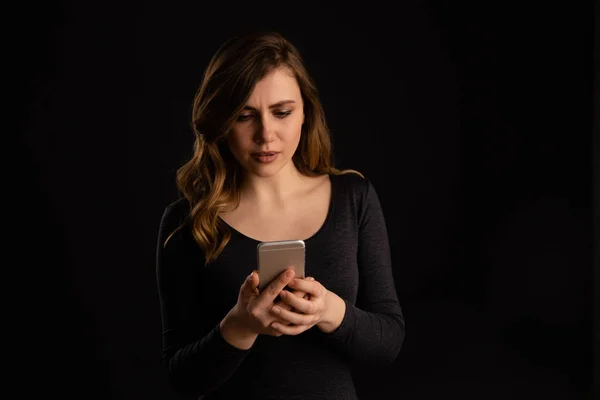 Femme sérieuse avec le téléphone dans sa main la regardant et textant avec le visage malheureux . — Photo