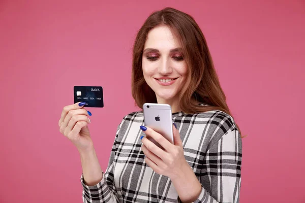 Happy woman holding credit card and phone standing isolated in the studio.