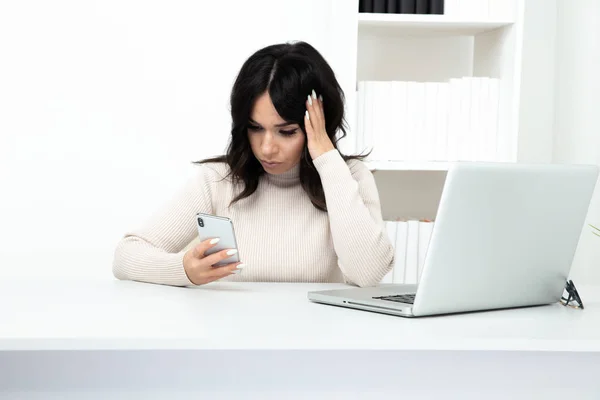 Unhappy and frustrated lady watching phone in office sitting infront of the computer.