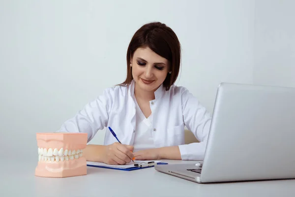 Woman dentist sitting at the table in office with dental staff isolated.
