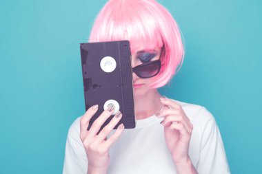 Gözlük ve mavi arka plan üzerinde siyah kaset tutan pembe peruk Retro kız.