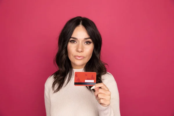Happy woman with credit card isolated in the pink studio.