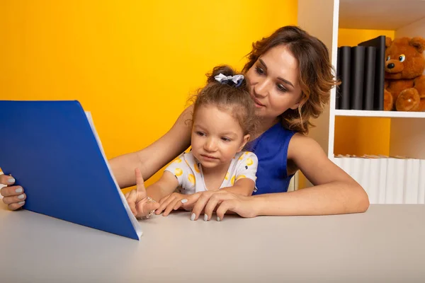 Moeder en dochter lezen zittend thuis aan tafel. — Stockfoto