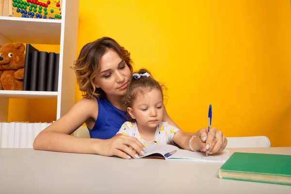 Bonita madre con linda hija sentada con libro en la habitación en casa . — Foto de Stock