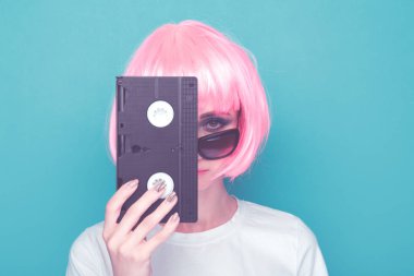 Gözlük ve mavi arka plan üzerinde siyah kaset tutan pembe peruk Retro kız.