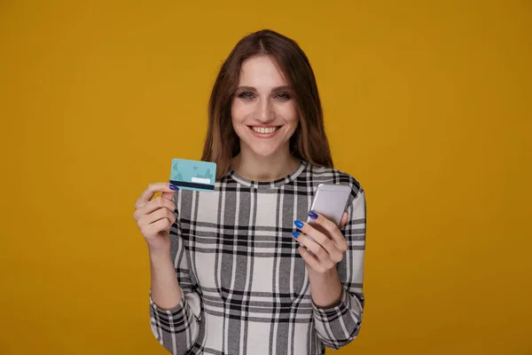 Młoda kobieta z telefonem i kartą kredytową stojący na białym tle w studiu. — Zdjęcie stockowe