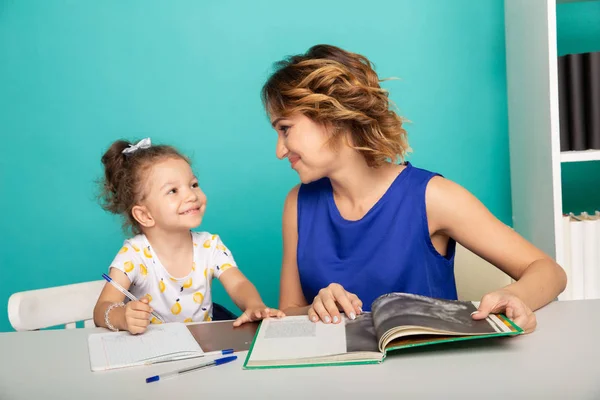 Mãe e filha sentadas na mesa fazendo lição de casa juntas. — Fotografia de Stock