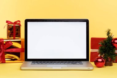 İnternetteki Noel alışverişi konsepti dizüstü bilgisayarda. Bilgisayarda beyaz ekran ve yanında kağıt torbalarla hediyeler..