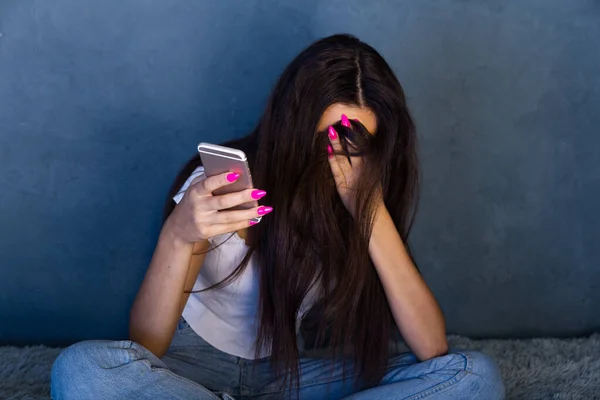 Mujer joven deprimida cerró la cara con la mano y sosteniendo el teléfono. Malo concepto en línea . — Foto de Stock