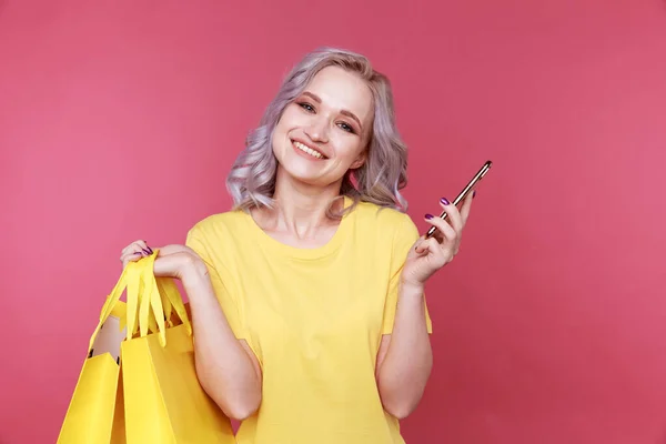 Mooie vrouwelijke persoon met telefoon en boodschappentassen aan de roze muur. — Stockfoto