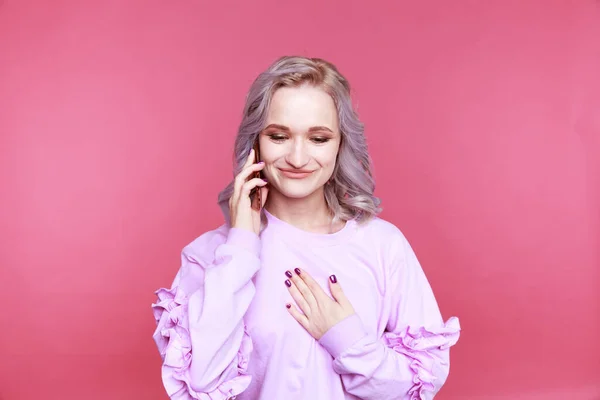 Šťastná dívka pomocí telefonu a s úsměvem stojící v růžovém studiu. — Stock fotografie