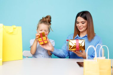 Küçük kızı olan yakışıklı anne mavi arka planda tek başına oturmuş hediyelerini topluyor..