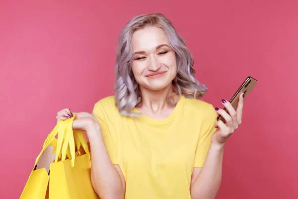 Jonge stijlvolle vrouw in de gele t-shurt holding telefoon en dezelfde solor packege geïsoleerd. — Stockfoto
