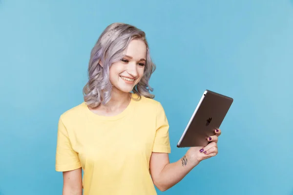 Šťastně se usmívající mladá žena drží tablet a pracuje v modrém studiu. — Stock fotografie