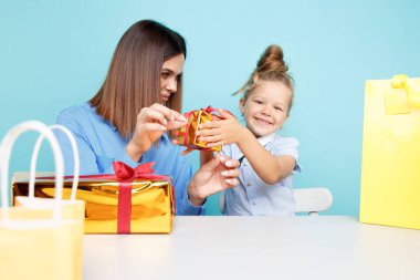 Küçük kızı olan yakışıklı anne mavi arka planda tek başına oturmuş hediyelerini topluyor..