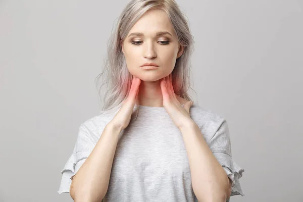 Honan kollar sköldkörteln själv. Närbild av kvinna i vit t-shirt vidrör halsen med röd fläck. Sköldkörtelrubbningar inkluderar struma, hypertyreoidea, hypotyreoidea, tumör eller cancer. Hälsovård. — Stockfoto