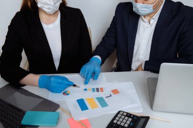 Ofiste çalışan iş adamları koruyucu maske ve eldiven takıyorlar. Salgın ve sosyal dışlanma döneminde önleyici tedbirler