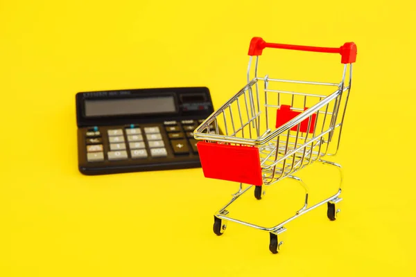 Compras inteligentes y ahorrar dinero concepto. Carrito de compras y calculadora sobre fondo amarillo —  Fotos de Stock