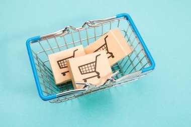 Mavi arka planda bir alışveriş sepetinde kutular. Tüketiciler için parmak uçlarıyla kolay alışveriş. Çevrimiçi alışveriş ve teslimat servisi.