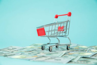 Para banknotları ve mavi arka planda alışveriş arabası. Tüketiciler için parmak uçlarıyla kolay alışveriş. Çevrimiçi alışveriş kavramı.
