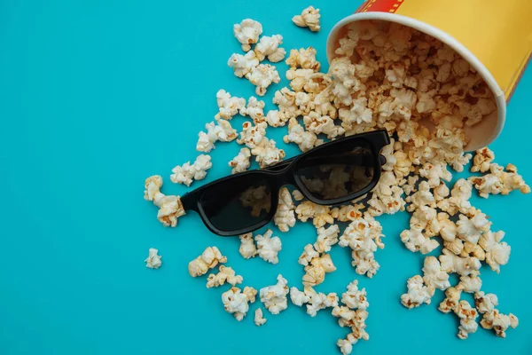 Z misky se vysypal popcorn. 3D brýle jsou na modrém pozadí. Koncept entainement — Stock fotografie