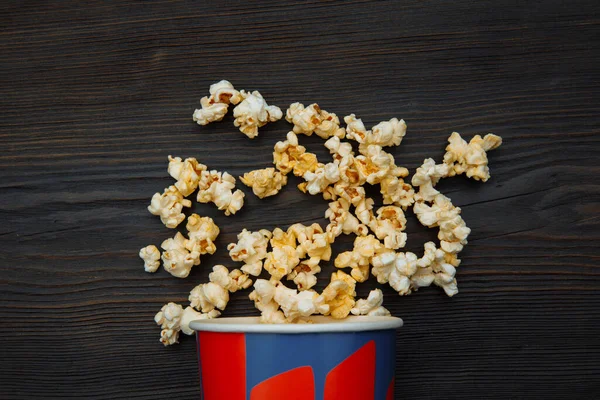 Popcorn spilldes från en ljus låda isolerad på trä bakgrund. Närbild ovanifrån — Stockfoto