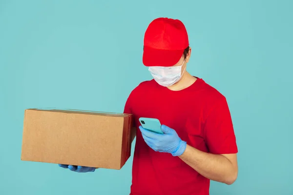 Courier in the red clothes holding big box and using phone in the blue case. — Stock Photo, Image