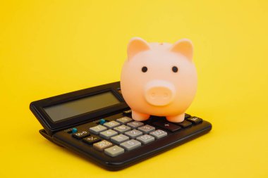 Pembe domuzcuk ya da bozuk para bankası ya da kumbara ya da para kutusu hesap makinesinde - sarı arka planda finans ve tasarruf kavramı