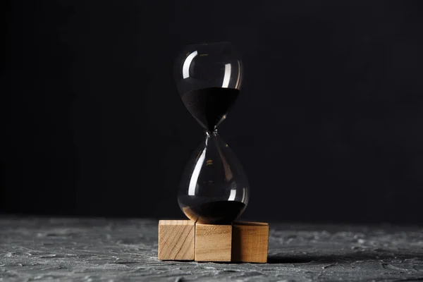 Reloj de arena o vidrio de arena en bloques de madera cubo, lugar para el texto, en la mesa de madera con fondo oscuro —  Fotos de Stock
