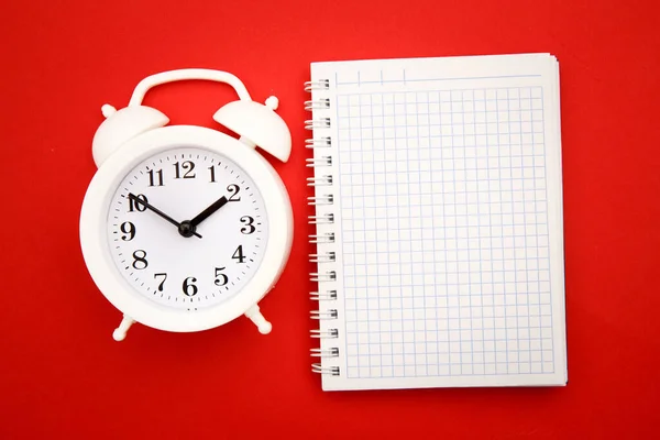 Reloj despertador blanco y cuaderno sobre fondo rojo, espacio vacío para texto —  Fotos de Stock
