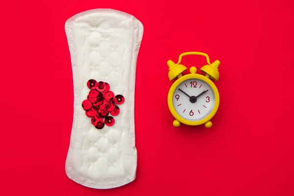 Foto de concepción médica. Almohadilla diaria y reloj amarillo sobre fondo rojo. Días críticos para la mujer, ciclo de menstruación ginecológica. Menstruación higiene sanitaria de la mujer —  Fotos de Stock