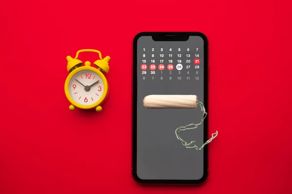 Mobile application to track your menstrual cycle and for marks. PMS and the critical days concept. Cotton tampon and yellow alarm clock on the red background