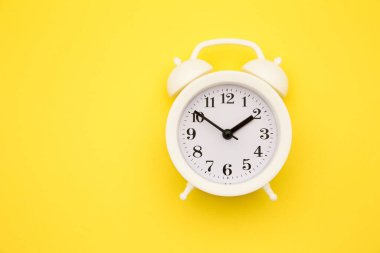 Sarı arka planda beyaz alarm saati izole edildi. Hayatın dinlenme saatleri. İyi sabahlar. Uyanık kalma kavramı..