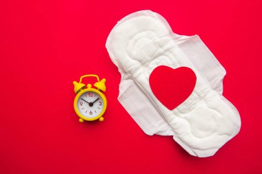 Kağıt kalpli kadın pedi ve kırmızı arka planda sarı alarm saati.