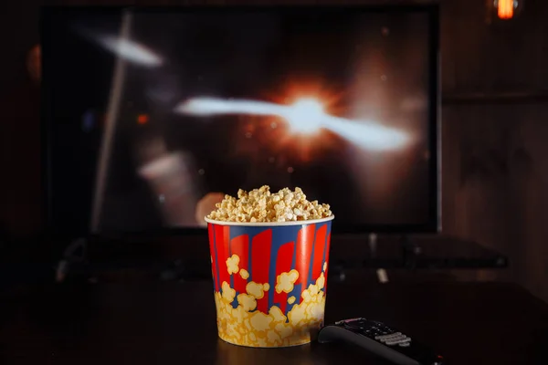 Miska popcornu na ciemnym stole i pilot TV z telewizorem. — Zdjęcie stockowe
