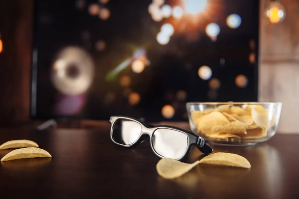 Chips y gafas 3D en el escritorio frente a un gran televisor . — Foto de Stock