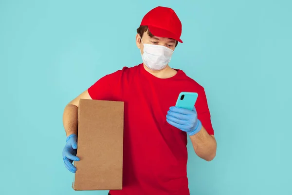 Courier in the red clothes holding big box and using phone in the blue case. — Stock Photo, Image